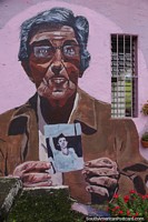 Man holds a photo of his son, mural on a pink building side in Medellin.